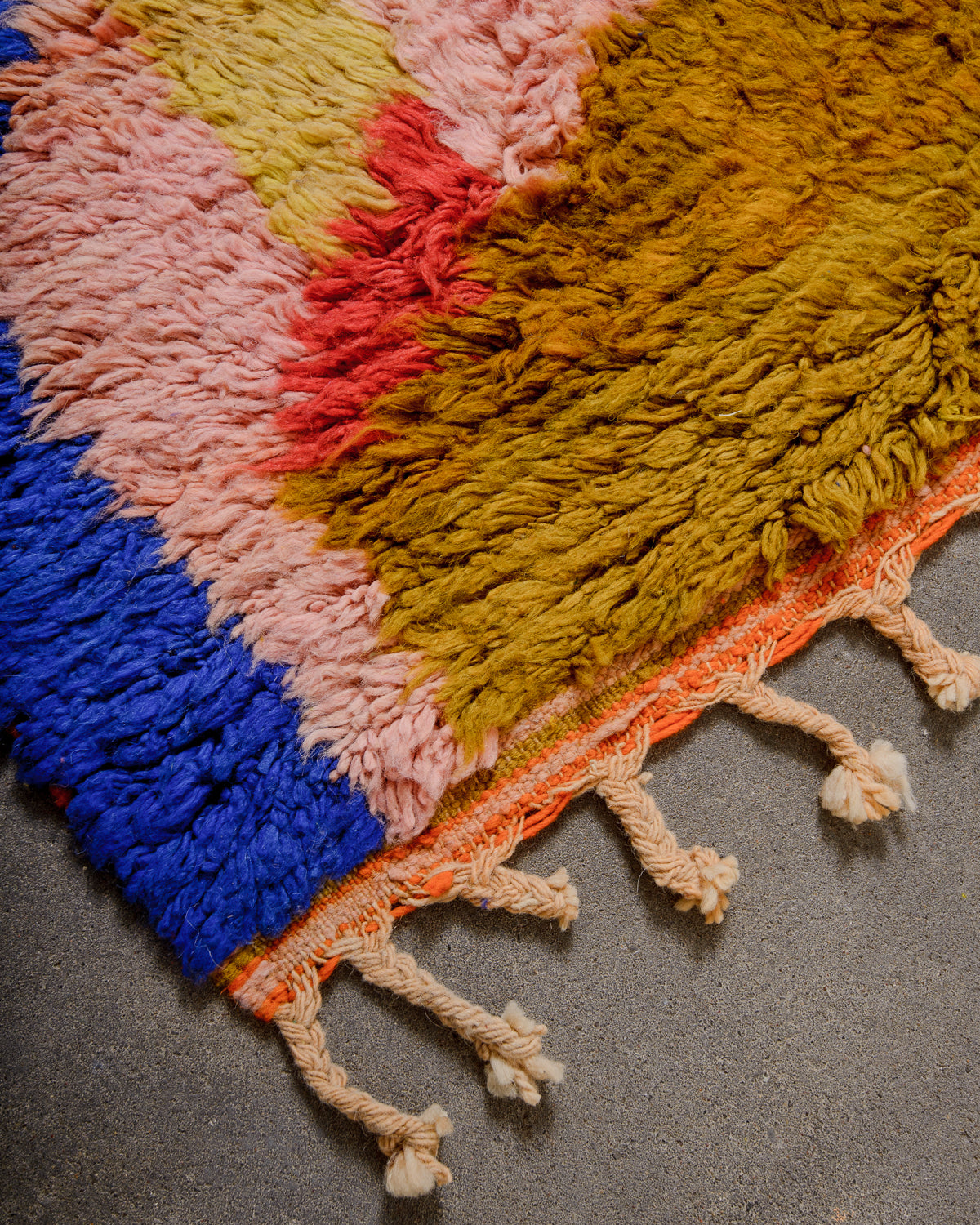 Corner of Berber runner rug with brightly coloured wool pile and natural wool tassels.